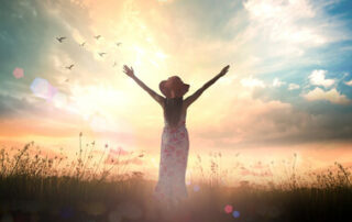 Woman holding her arms out to the sky in front of a sunrise