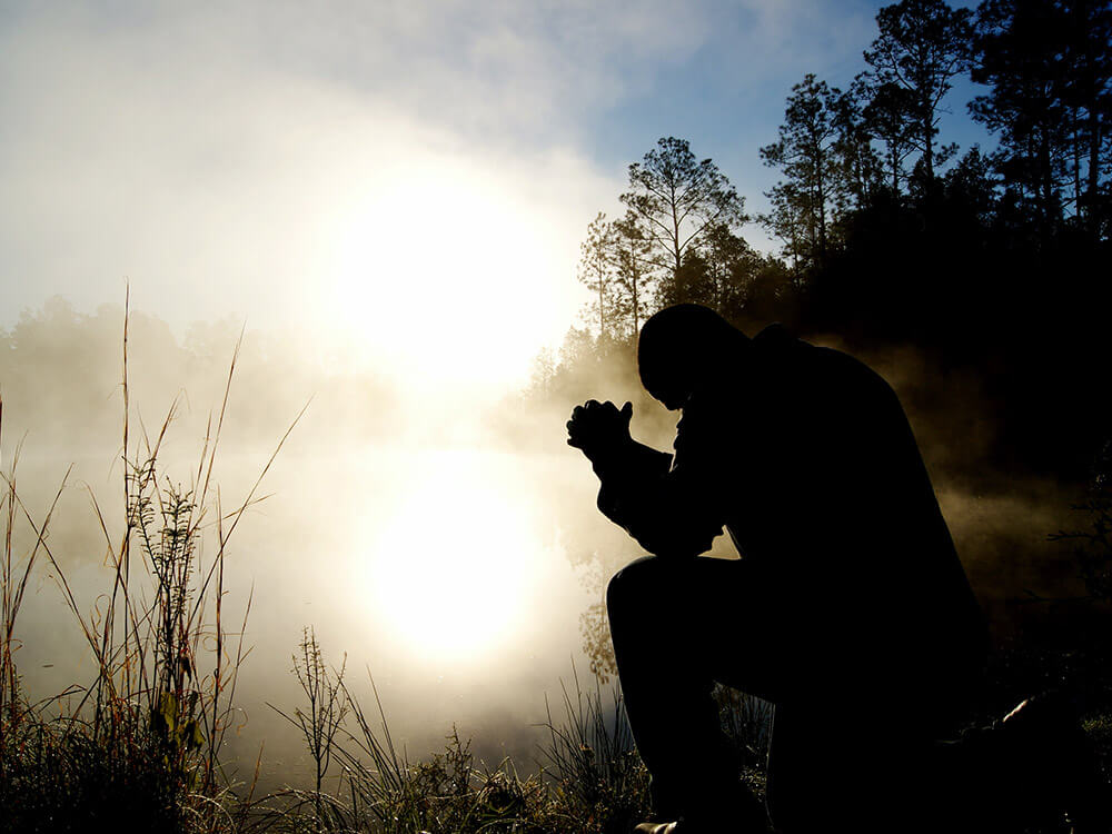 Man outdoors kneeling in prayer