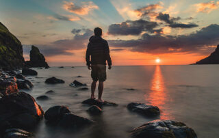 Man standing on rock overlooking the ocean with sunset in the background